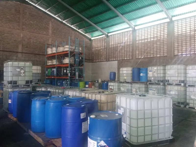 Galpón con estantes, tambores azules y contenedores IBC almacenados sobre paletas