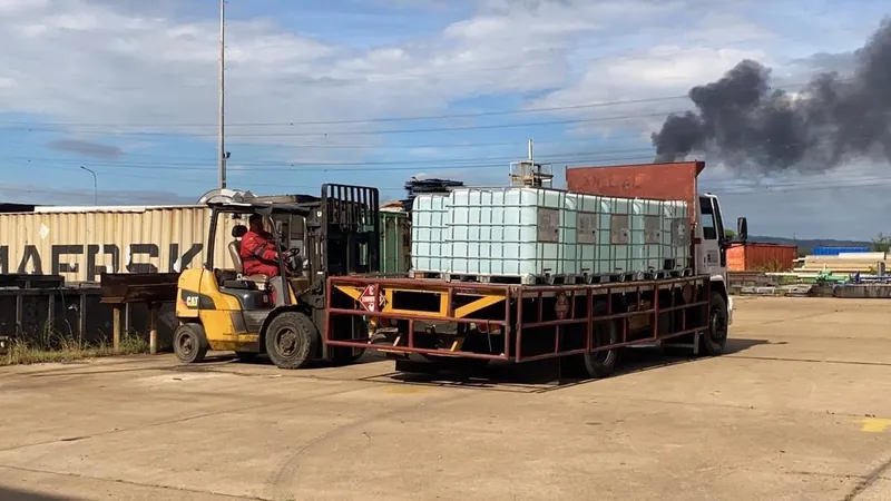 Montacargas amarillo cargando un contenedor IBC sobre la plataforma de un camión en un patio industrial