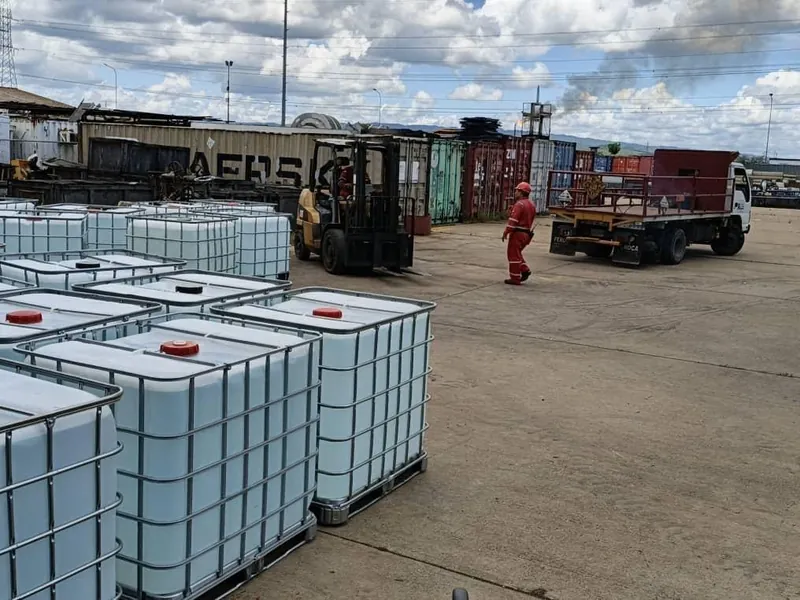 Contenedores IBC en primer plano y un montacargas con un camión al fondo en un patio industrial