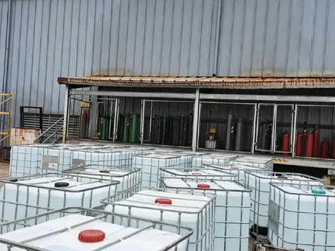 Contenedores IBC blancos frente a un galpón metálico con cilindros de gas en jaulas