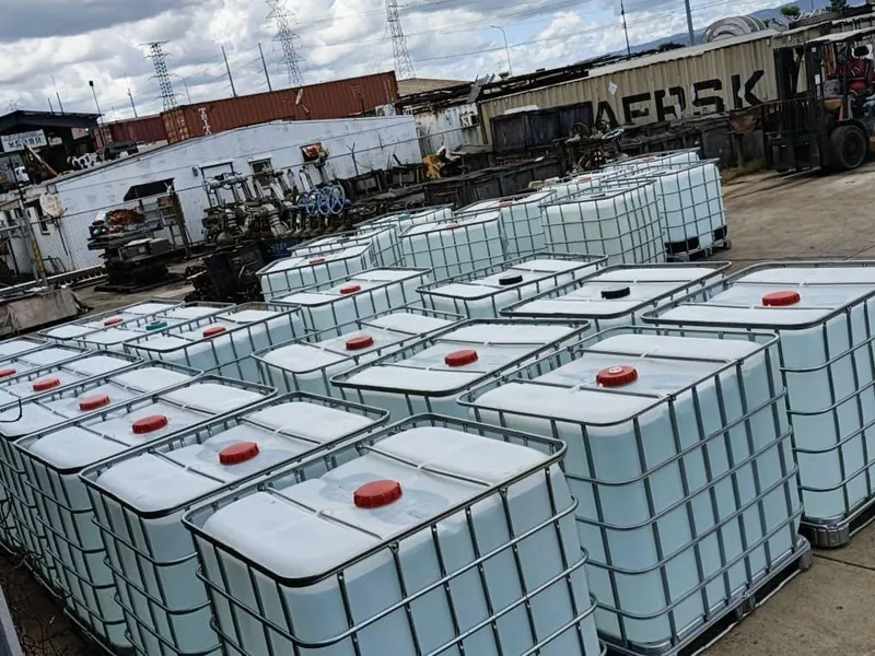 Contenedores IBC blancos alineados en un patio de concreto, con un montacargas al fondo